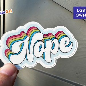 May include: A rainbow-colored sticker with the word "Nope" in white, with the text "LGBTQ OWNED" in the upper right corner.