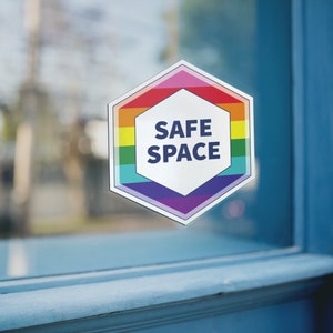 May include: A hexagonal sticker with a rainbow border and the words "SAFE SPACE" in white text on a white background.