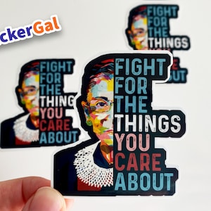 May include: A die-cut vinyl sticker featuring a colorful pop-art portrait of Ruth Bader Ginsburg on the left and the text FIGHT FOR THE THINGS YOU CARE ABOUT in bold, distressed lettering on the right, set against a dark background.