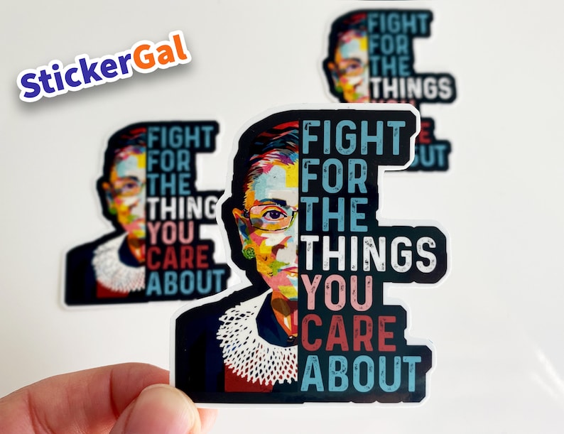 May include: A die-cut vinyl sticker featuring a colorful pop-art portrait of Ruth Bader Ginsburg on the left and the text FIGHT FOR THE THINGS YOU CARE ABOUT in bold, distressed lettering on the right, set against a dark background.