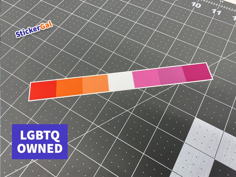 May include: A rectangular sticker featuring a horizontal gradient of seven distinct color bands, transitioning from dark red, orange, light orange, white, light pink, medium pink, to dark pink. The sticker is positioned on a dark gray cutting mat.