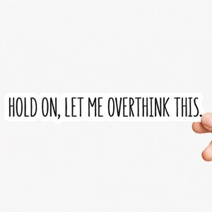 May include: A rectangular white sticker featuring the black text "HOLD ON, LET ME OVERTHINK THIS." in a clean, sans-serif font. The sticker has a thin white border around the lettering, creating a simple and clear design for various surfaces.
