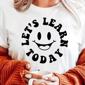 May include: White t-shirt with a black graphic that says "Let's Learn Today" with a smiley face in the centre.