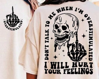 May include: A white t-shirt with a black skull and skeleton hand graphic on the back. The graphic says "Don't talk to me when I'm overstimulated. I will hurt your feelings."