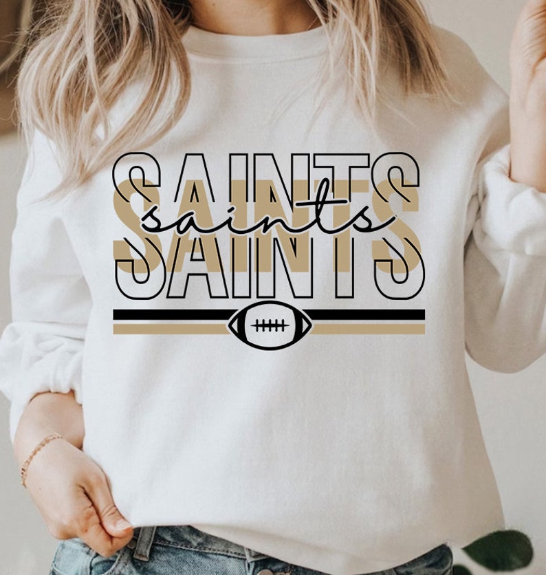 May include: White sweatshirt with a black and gold graphic design featuring the word "Saints" repeated three times with a football in the center.