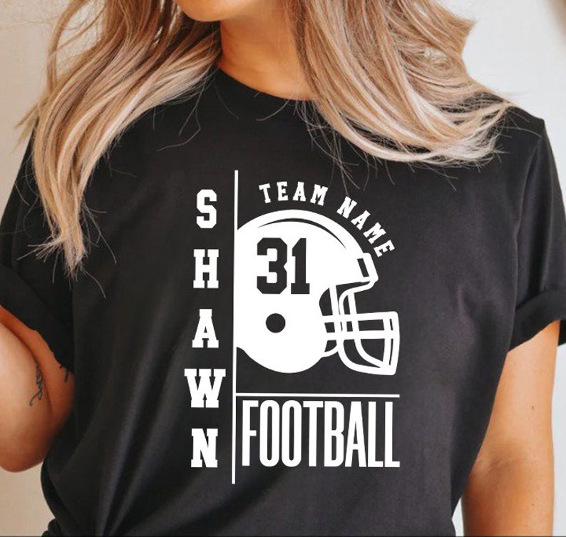 May include: Black t-shirt with white text that reads "SHAWN" and "TEAM NAME" with a football helmet graphic and the number "31". The text "FOOTBALL" is also printed in white.