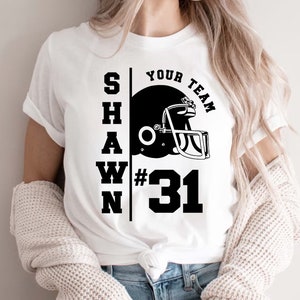 K&ouml;nnte beinhalten: Wei&szlig;es T-Shirt mit schwarzem Text "SHAWN YOUR TEAM #31" und einer Grafik eines schwarzen und wei&szlig;en Footballhelms.