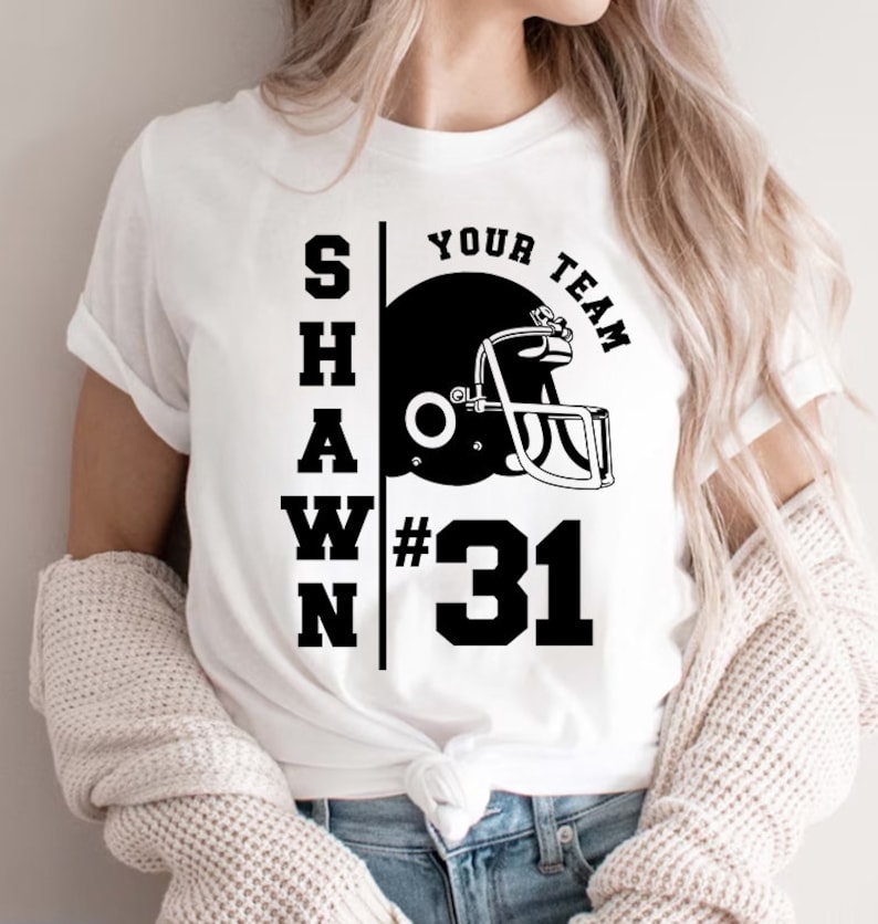 K&ouml;nnte beinhalten: Wei&szlig;es T-Shirt mit schwarzem Text "SHAWN YOUR TEAM #31" und einer Grafik eines schwarzen und wei&szlig;en Footballhelms.