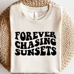 Könnte beinhalten: Ein weißes T-Shirt mit dem Text "FOREVER CHASING SUNSETS" in schwarzer Schrift in einer Retro-Schriftart.