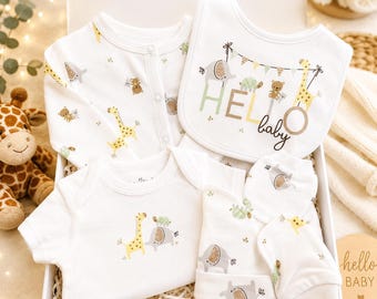 May include: A white baby gift set featuring a onesie, long-sleeve shirt, bib, hat, and socks. The set is decorated with giraffe, elephant, and teddy bear graphics. The bib reads "Hello Baby". The set is presented in a white box.
