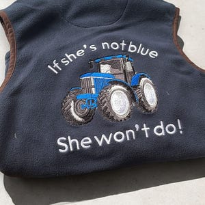 May include: A blue fleece vest with a white embroidered tractor and the text "If she's not blue she won't do!"