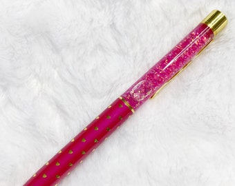 May include: A pink pen with gold accents and a clear section filled with pink glitter. The pen has a gold cap and a gold tip.
