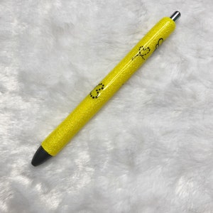 May include: A yellow glitter pen with black ink and a silver clip. The pen has a black smiley face and a black heart design on it.