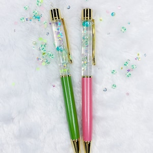 May include: Two clear pens with gold accents and glitter inside. One pen is green and the other is pink.