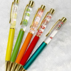 May include: Five colorful pens with gold accents and clear barrels filled with fruit slices. The pens are yellow, green, orange, red, and teal.