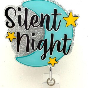 May include: A badge reel with the words "Silent Night" in black script over a light blue crescent moon shape. The moon is surrounded by silver glitter, with three yellow stars. A clear plastic clip and retractable cord are attached.
