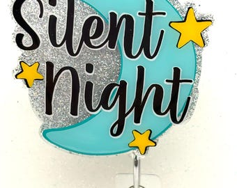 May include: A badge reel with the words "Silent Night" in black script over a light blue crescent moon shape. The moon is surrounded by silver glitter, with three yellow stars. A clear plastic clip and retractable cord are attached.