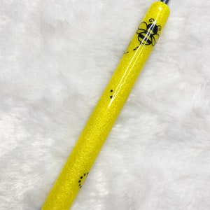 May include: A yellow glitter pen with a black bee design. The pen has a black ink tip and a silver clip.