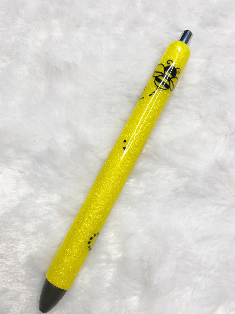 May include: A yellow glitter pen with a black bee design. The pen has a black ink tip and a silver clip.