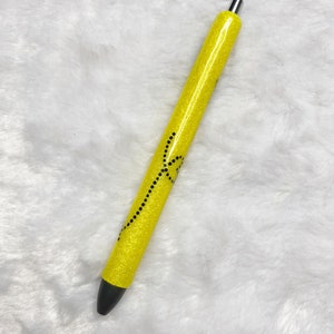 May include: A yellow glitter pen with a black design. The pen has a silver cap.