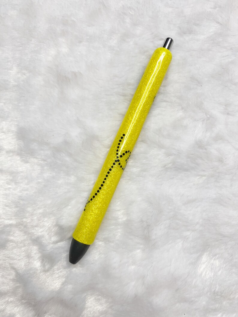 May include: A yellow glitter pen with a black design. The pen has a silver cap.