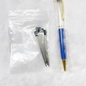 May include: A clear plastic bag containing six silver pen refills with black tops. A blue and gold pen is next to the bag.