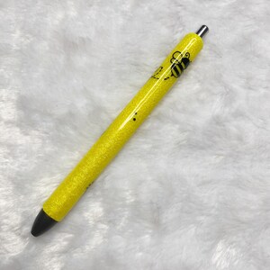 May include: A yellow glitter pen with a black bee design. The pen has a silver clip and a black tip.