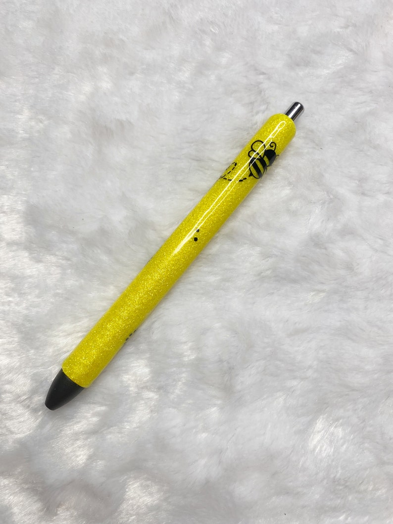 May include: A yellow glitter pen with a black bee design. The pen has a silver clip and a black tip.