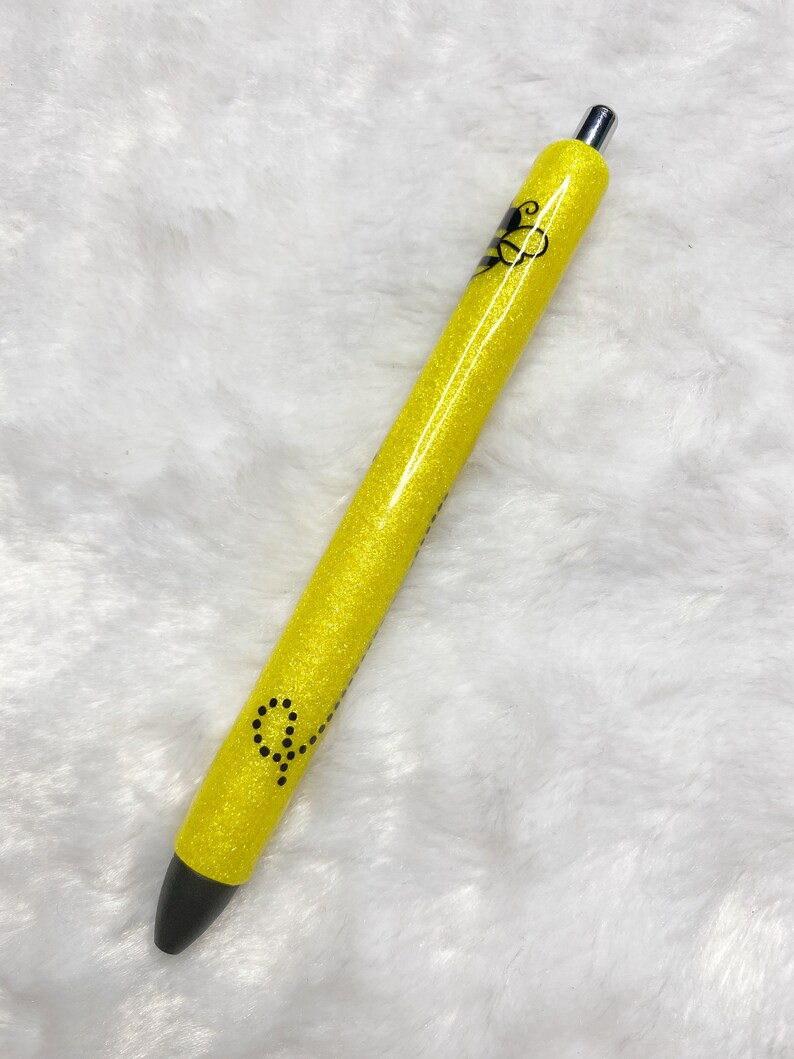 May include: A yellow glitter pen with a black bee design and black dots. The pen has a silver clip.