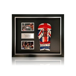 Op de afbeelding: Ingelijfde bokshandschoen met een Union Jack-ontwerp, gesigneerd door Tyson Fury, de 'Gypsy King'. Inclusief twee actiefoto's en een plaatje met de tekst 'Personally Signed by Tyson Fury World Champion'. De lijst is zwart met een zilveren rand.