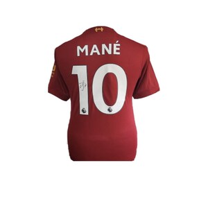 May include: A red football shirt with the name "MAN&Eacute;" and the number "10" on the back. The shirt has a white Liverpool crest on the left chest and a white Adidas logo on the right chest.