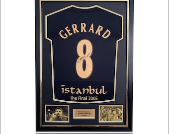 Op de afbeelding: Ingelijst marineblauw voetbalshirt met "GERRARD" en het nummer "8" in goud. Daaronder staat "istanbul the Final 2005". Inclusief twee kleine foto's en een gesigneerde plaquette. De lijst is zwart met een gouden binnenrand.
