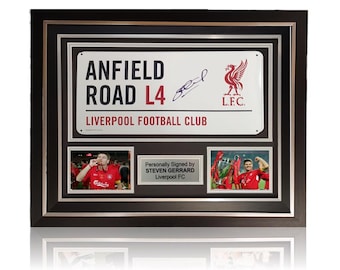 May include: A framed print of a white sign with the text "Anfield Road L4 Liverpool Football Club" and a red Liverpool FC crest. The sign is signed by Steven Gerrard. The frame is black with a silver border and includes two photos of Gerrard.