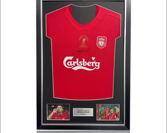 Könnte beinhalten: Gerahmtes rotes Liverpool FC-Trikot mit dem Carlsberg-Logo, einem Wappen und einer Unterschrift. Der Rahmen enthält zwei kleine Fotos und den Text "Personally Signed by STEVEN GERRARD Liverpool". Das Trikot wird auf schwarzem Hintergrund präsentiert.
