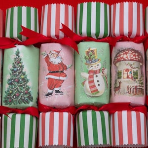 May include: Six Christmas crackers arranged in two rows, featuring festive illustrations of a deer, a Christmas tree, Santa Claus, a snowman, a mushroom house, and a kitten. Each cracker has green and white striped ends tied with red ribbons.