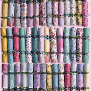 Puede incluir: Una colección de 36 crackers de Navidad de papel coloridos con varios patrones, incluyendo diseños florales, de lunares y geométricos. Los crackers están atados con cinta verde y rosa.
