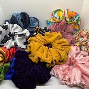 May include: A collection of colourful hair scrunchies in various fabrics and patterns, including floral, polka dot, and solid colours. The scrunchies are made of soft, stretchy material and are perfect for holding hair in place.