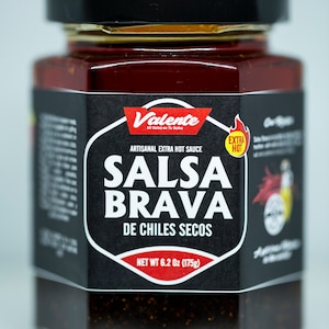 May include: A glass jar of "Salsa Brava" artisanal extra hot sauce. The label is black with white and red text, including "Valente" and "Extra Hot." The jar contains a dark red, chunky sauce. Net weight is 6.2 oz (175g).