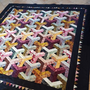 Puede incluir: Una colcha negra con un patrón geométrico de triángulos coloridos. La colcha está hecha de tela con estampado floral. La colcha tiene un borde negro con un borde festoneado.