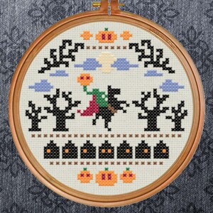 May include: A cross-stitch embroidery hoop with a Halloween scene. The design features a black cat flying on a broomstick with a witch, a full moon, clouds, trees, and pumpkins.