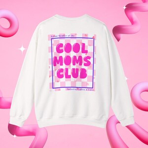 Könnte beinhalten: Weißes Sweatshirt mit dem Text "COOL MOMS CLUB" in rosa Buchstaben in einer rosa-lila karierten Box. Der Text "Proud Member of the" steht darüber und "Fueled by Coffee & Love" darunter.
