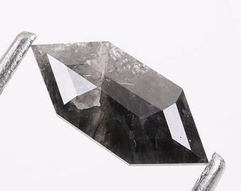 Może przedstawiać: Szlifowany, sześciokątny diament w kolorze ciemnoszarym z ostrym zakończeniem. Diament jest trzymany w pęsecie.