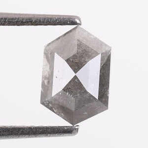 Op de afbeelding: Een grijze, zeshoekige, gefacetteerde diamant met een wit, kruisvormig patroon in het midden.