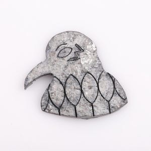 May include: A gray, bird-shaped decorative object with a long beak and a series of leaf-like shapes along the bottom. The bird's eye and a lightning bolt are outlined in black. The object has a textured surface.