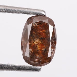 May include: A brown oval-shaped diamond with a faceted cut. The diamond has a dark brown color with inclusions.
