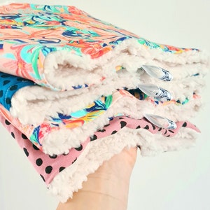 K&ouml;nnte beinhalten: Ein Stapel aus vier Stoff-Spuckt&uuml;chern f&uuml;r Babys mit einer wei&szlig;en Sherpa-R&uuml;ckseite. Die T&uuml;cher haben verschiedene Muster, darunter Blumen, Paisley und Punkte.