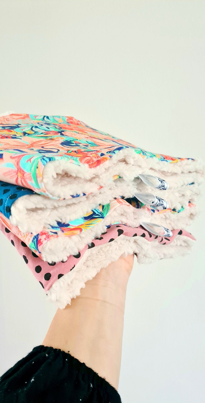 K&ouml;nnte beinhalten: Ein Stapel aus vier Stoff-Spuckt&uuml;chern f&uuml;r Babys mit einer wei&szlig;en Sherpa-R&uuml;ckseite. Die T&uuml;cher haben verschiedene Muster, darunter Blumen, Paisley und Punkte.