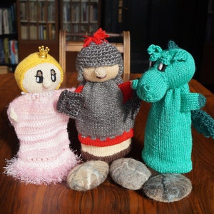 Könnte beinhalten: Drei gestrickte Fingerpuppen: eine rosa Prinzessin mit einer goldenen Krone, ein grauer Ritter mit einem roten Umhang und ein grüner Drache.