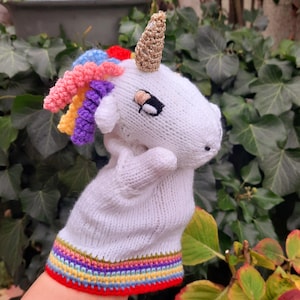 Könnte beinhalten: Weißer gestrickter Einhorn-Handpuppe mit einer Regenbogenmähne und einem goldenen Horn. Die Puppe hat einen rot, gelb, grün, blau und violett gestreiften Manschetten.