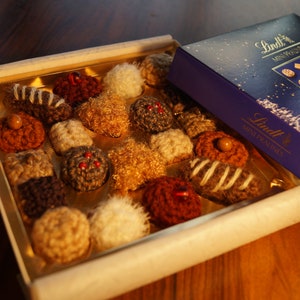 Op de afbeelding: Een doos Lindt Mini Pralines met een selectie van chocoladetruffels. De doos is blauw met een wit sterrenpatroon en het Lindt-logo. De truffels zijn gerangschikt in een doos met een witte achtergrond.